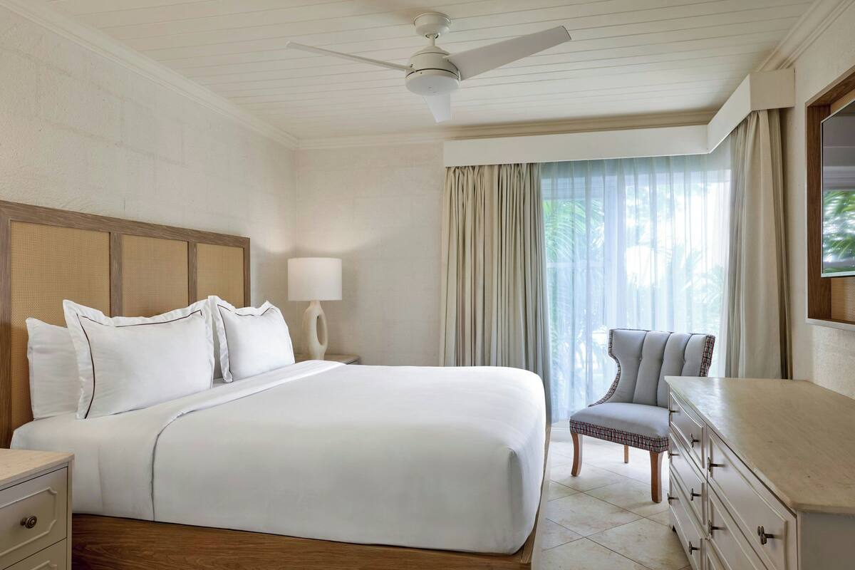 Ein Hotelzimmer mit einem Bett, einem Sessel, einer Kommode, einer Lampe und einem Deckenventilator.