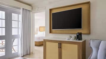 Une chambre d’hôtel dotée d’une grande fenêtre, d’un téléviseur à écran plat fixé au mur, d’une armoire en bois, d’un canapé et d’un lit avec une tête de lit.