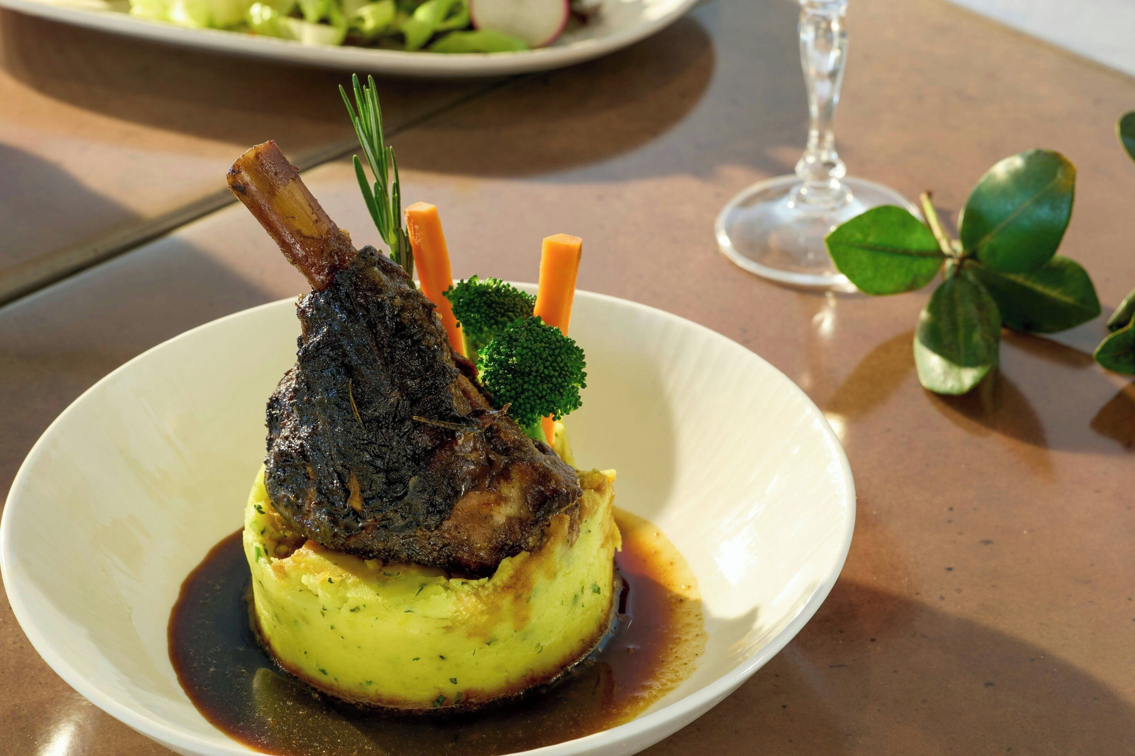 A plate of food with a lamb shank, mashed potatoes, and vegetables.