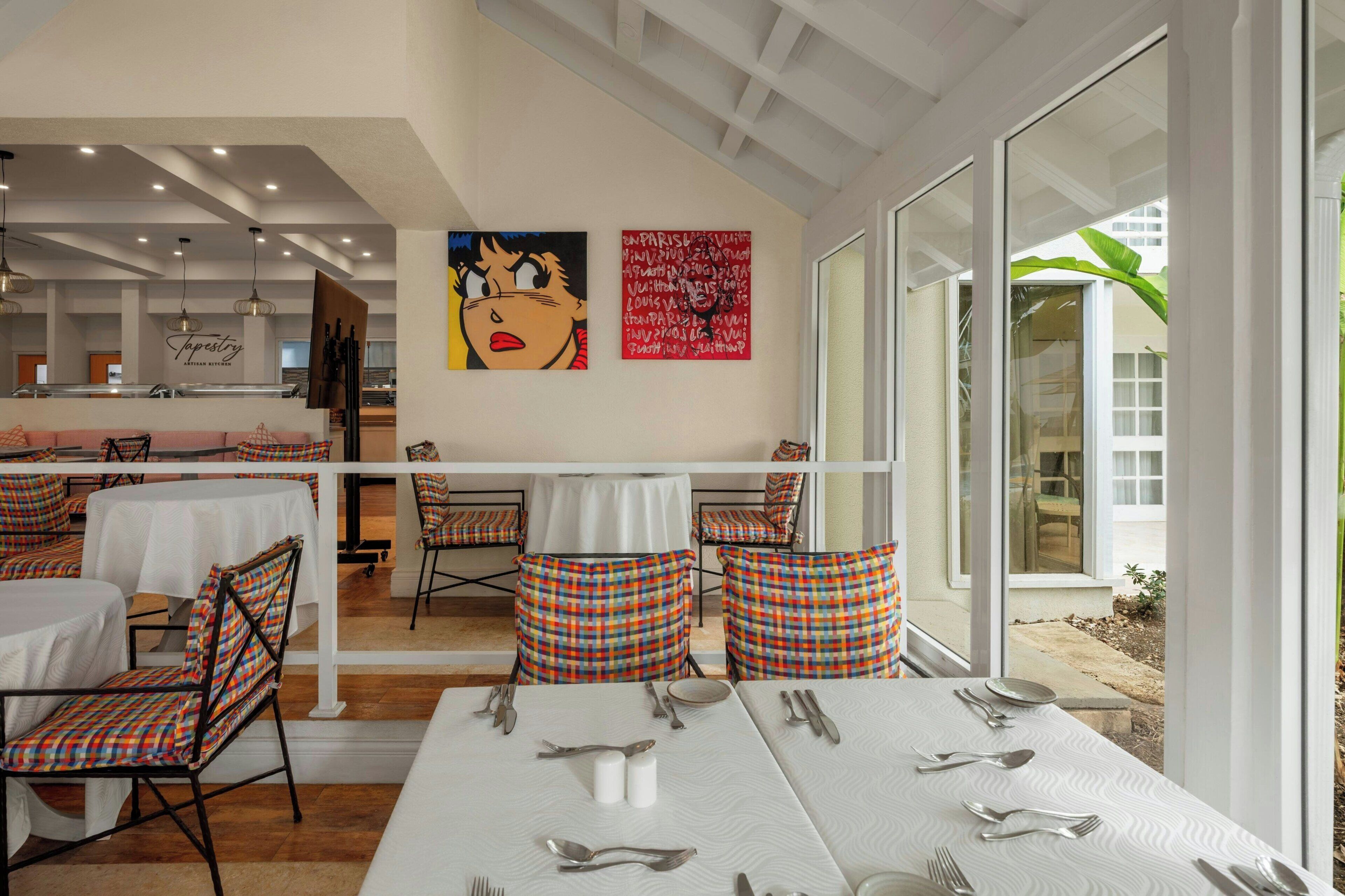 Een restaurant met een lange eettafel, gedekt voor een maaltijd, omringd door stoelen met kleurrijke kussens.