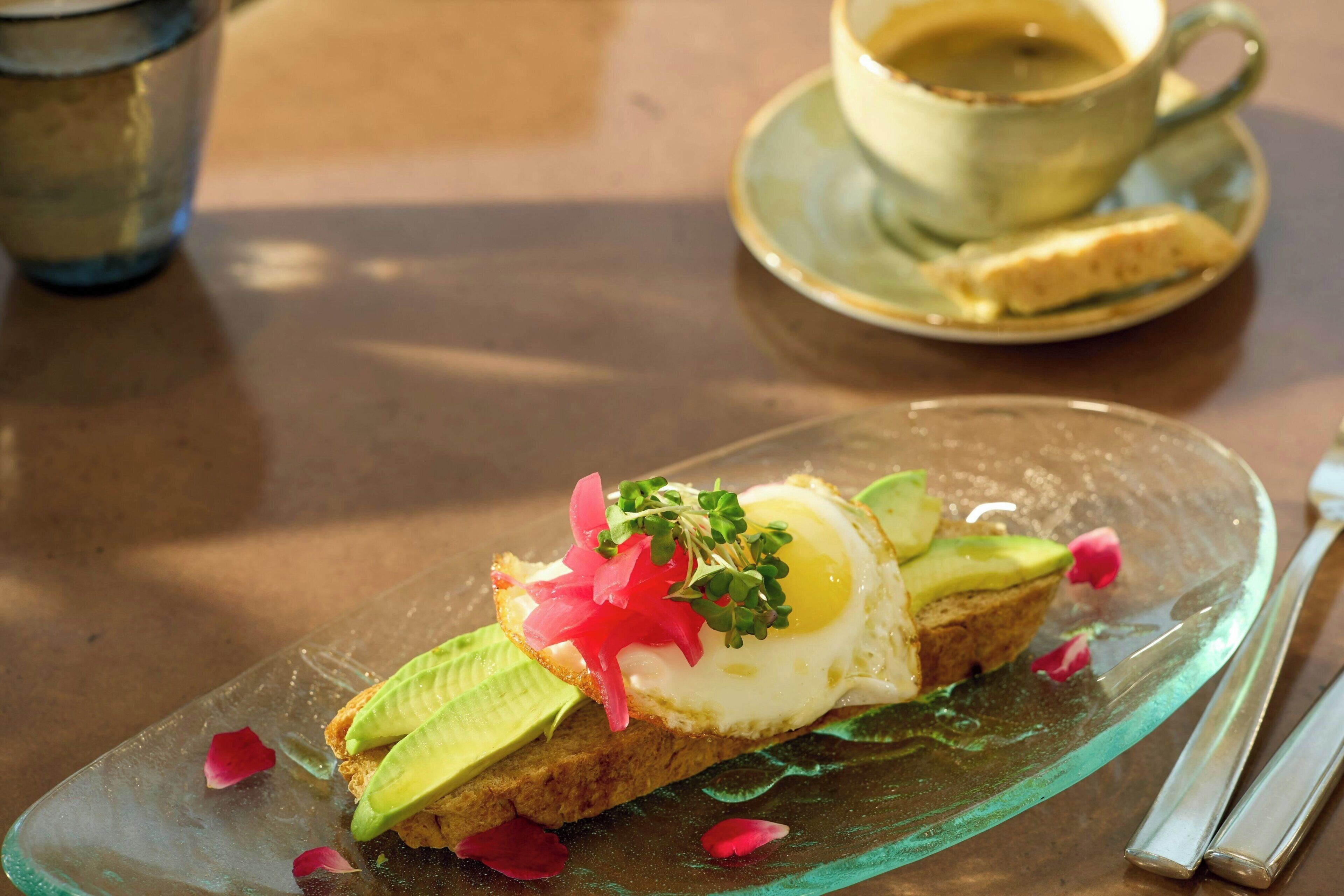 Un plato de desayuno con tostadas, aguacate, un huevo frito y adornos sobre un plato de vidrio.