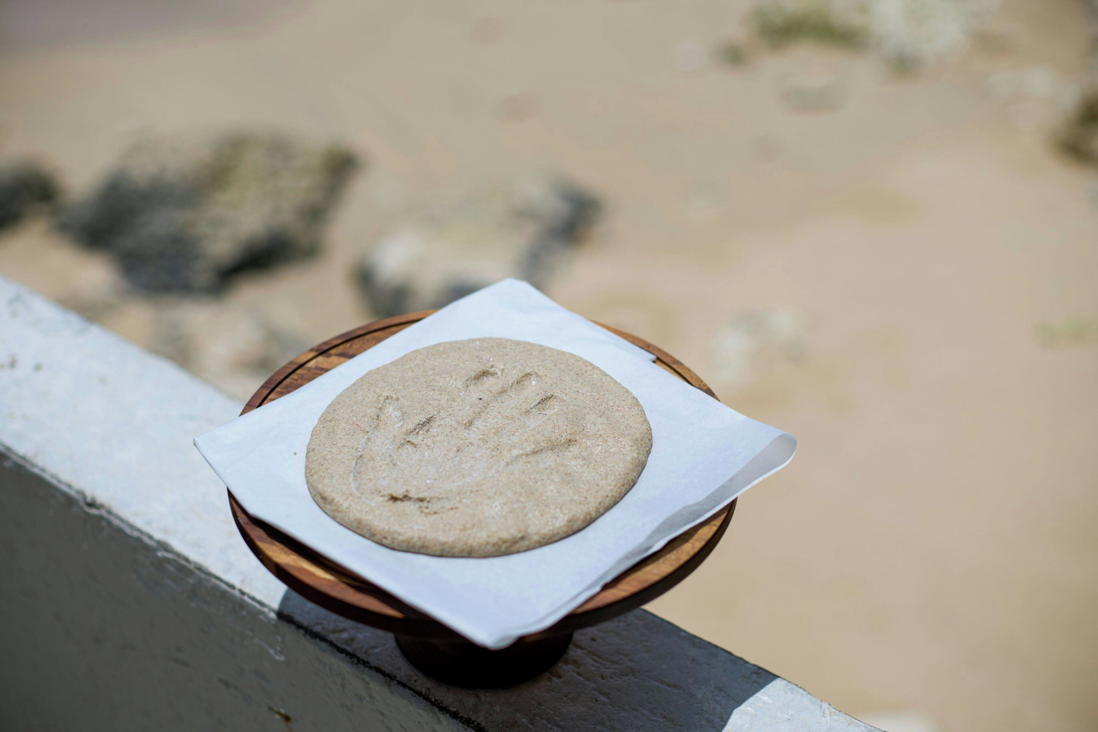 A round, flat object on a wooden tray with a white paper underneath, placed on a railing.