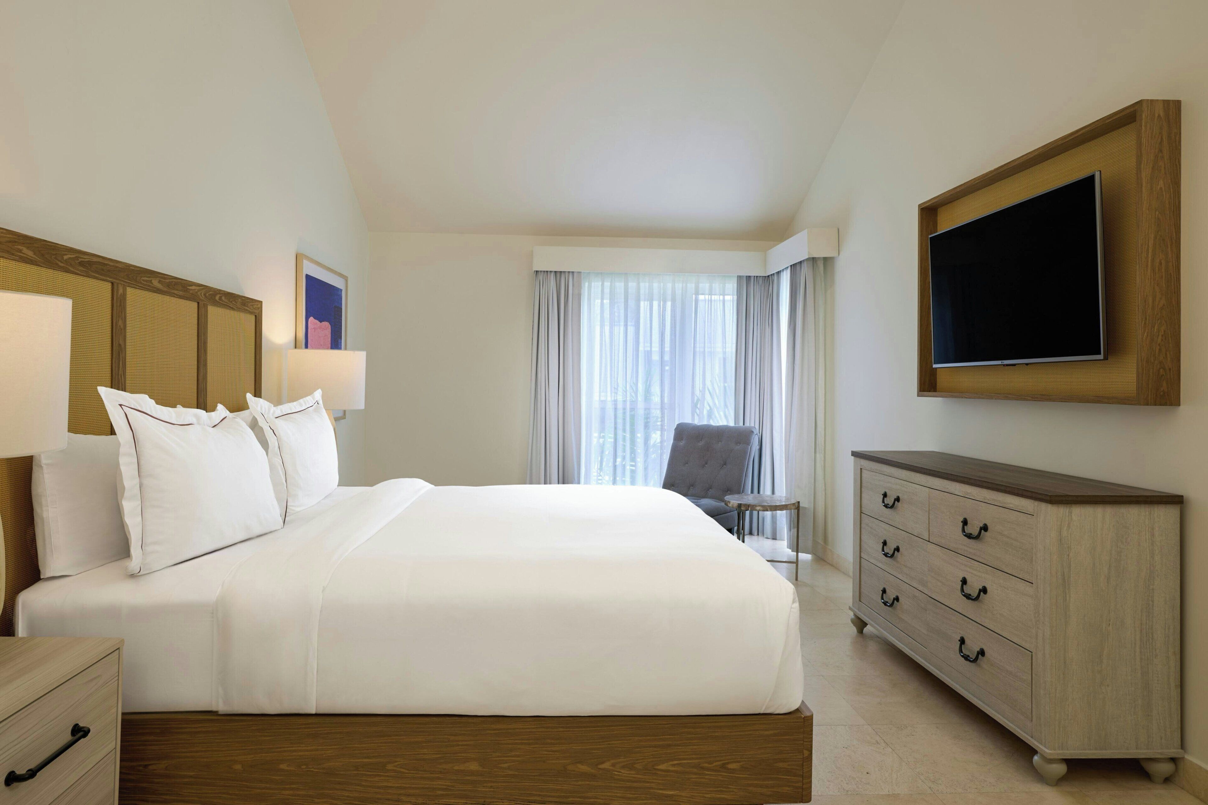 A hotel room with a bed, a TV, a dresser, and a chair.