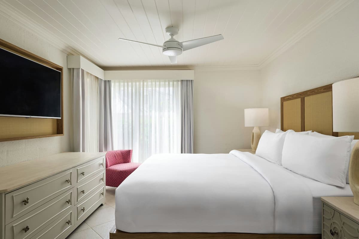 Ein Hotelzimmer mit Bett, Schreibtisch, Stuhl, Deckenventilator und einem an der Wand montierten Fernseher.