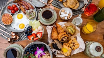 A breakfast spread with eggs, bacon, toast, fruits, and beverages on a wooden table.