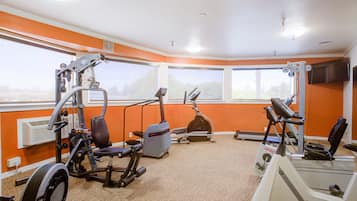 Un gimnasio con diversas máquinas de ejercicio, ventanas amplias y una televisión de pantalla plana.
