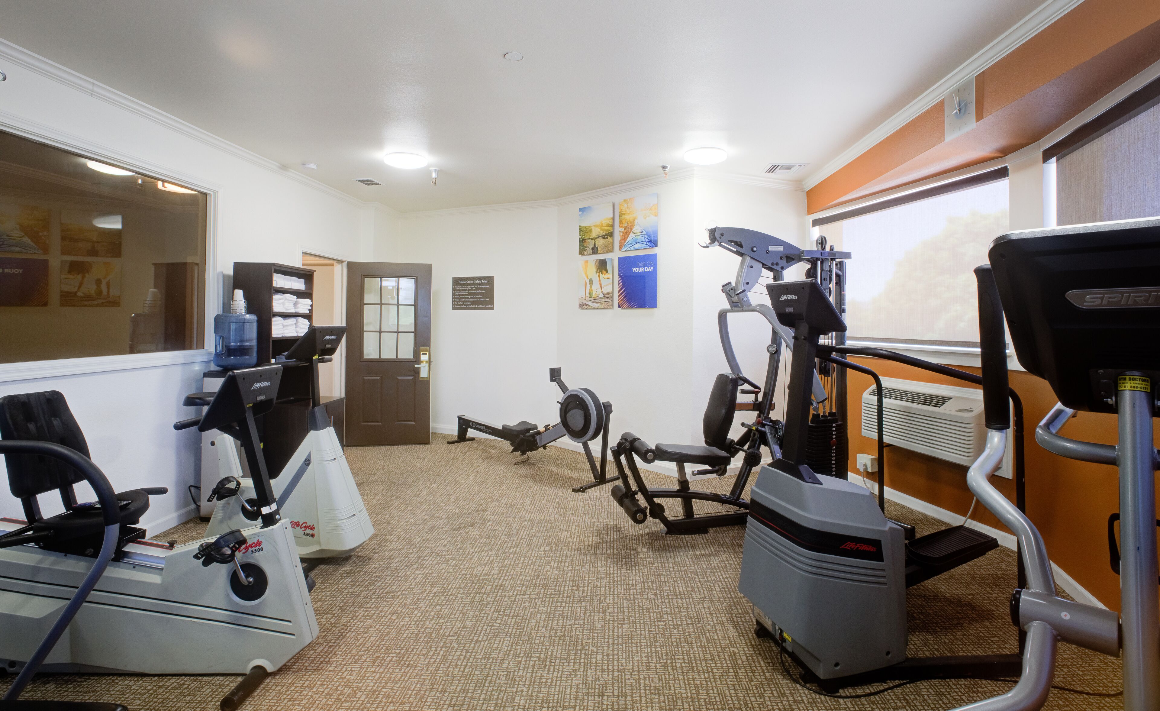 A fitness center with cardio machines, a weight bench, and a wall-mounted air conditioning unit.