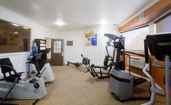 A fitness center with cardio machines, a weight bench, and a wall-mounted air conditioning unit.