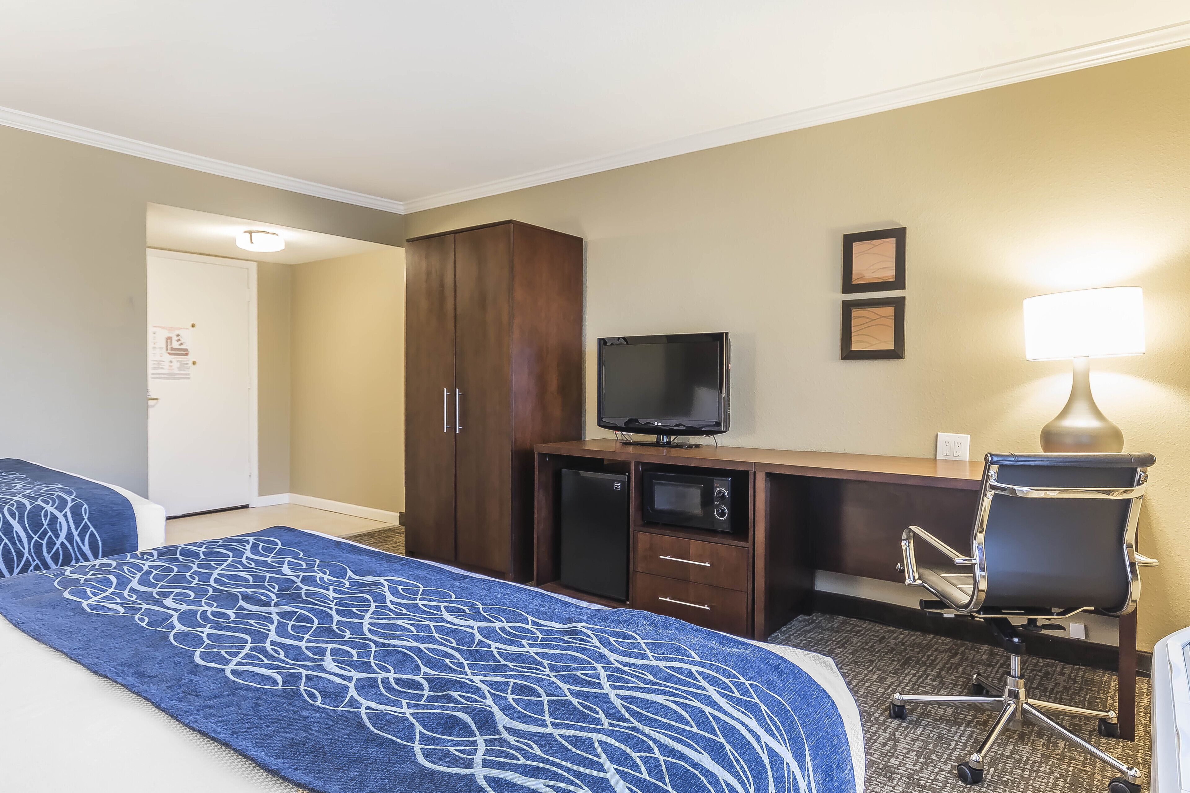 A hotel room with two beds, a desk with a television, a refrigerator, a microwave, a desk lamp, and a chair.