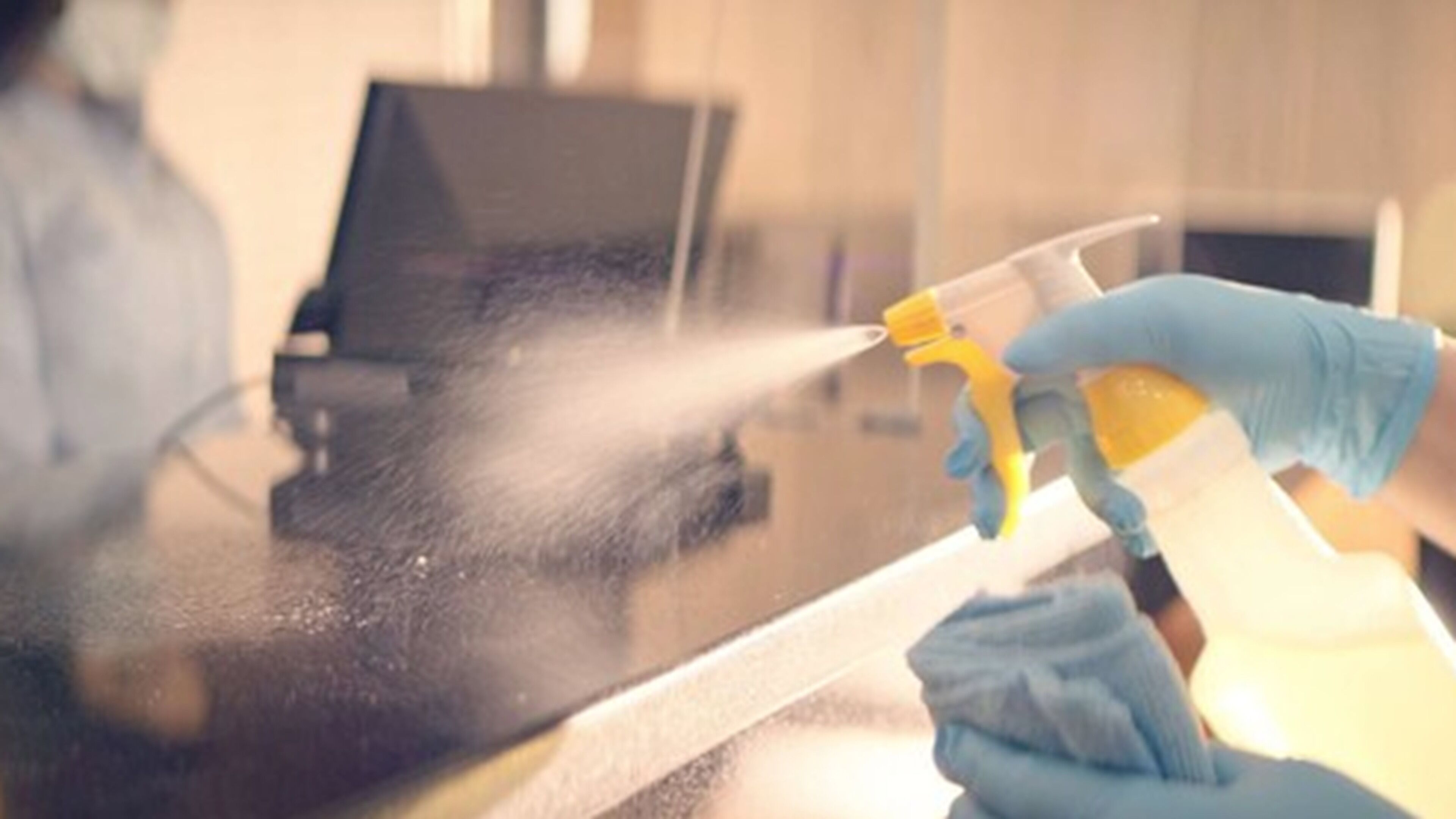 A person wearing blue gloves using a spray bottle to clean a glass surface.