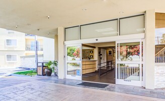 A hotel entrance with a glass door, a staircase leading inside, and a view of the surrounding buildings.