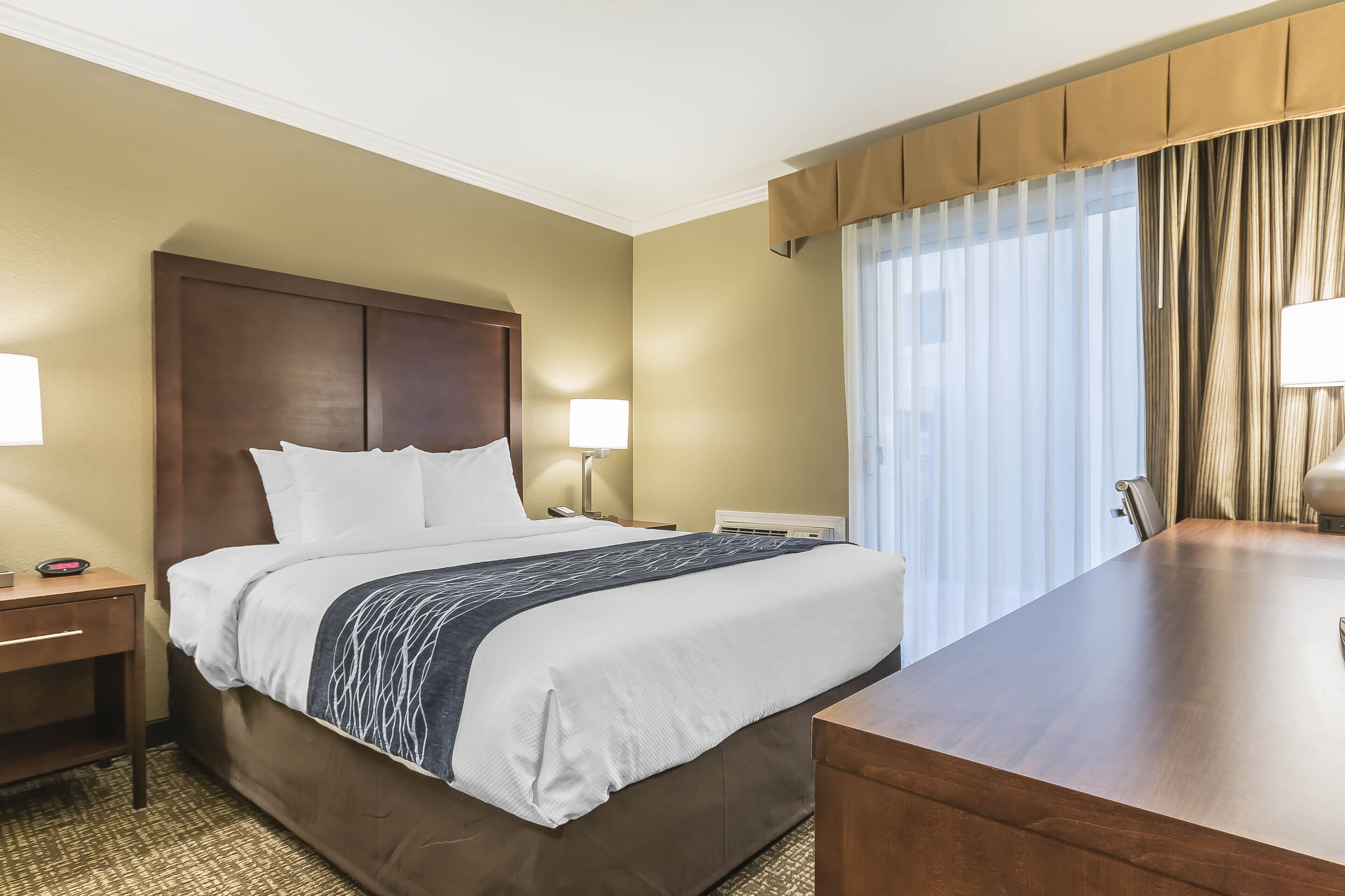 A hotel room with a large bed, bedside tables, a desk, and a window with curtains.