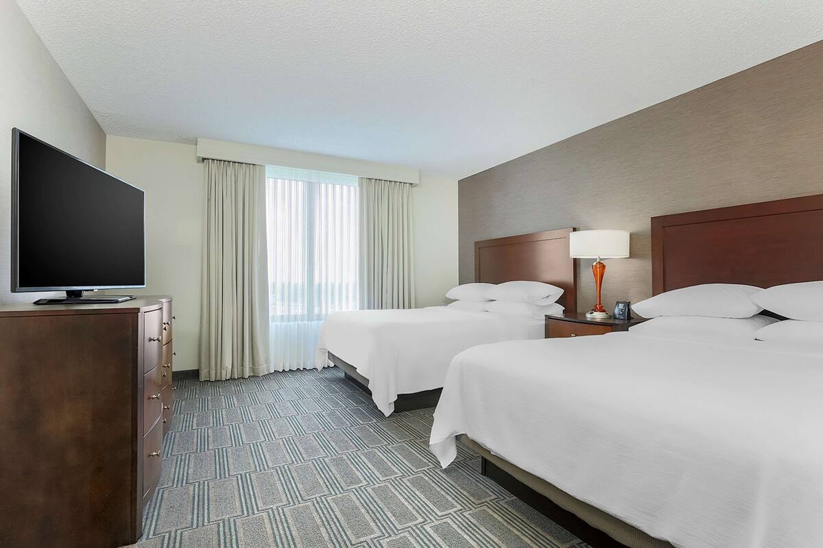 Une chambre d’hôtel avec deux lits, un téléviseur posé sur une commode et une fenêtre avec des rideaux.
