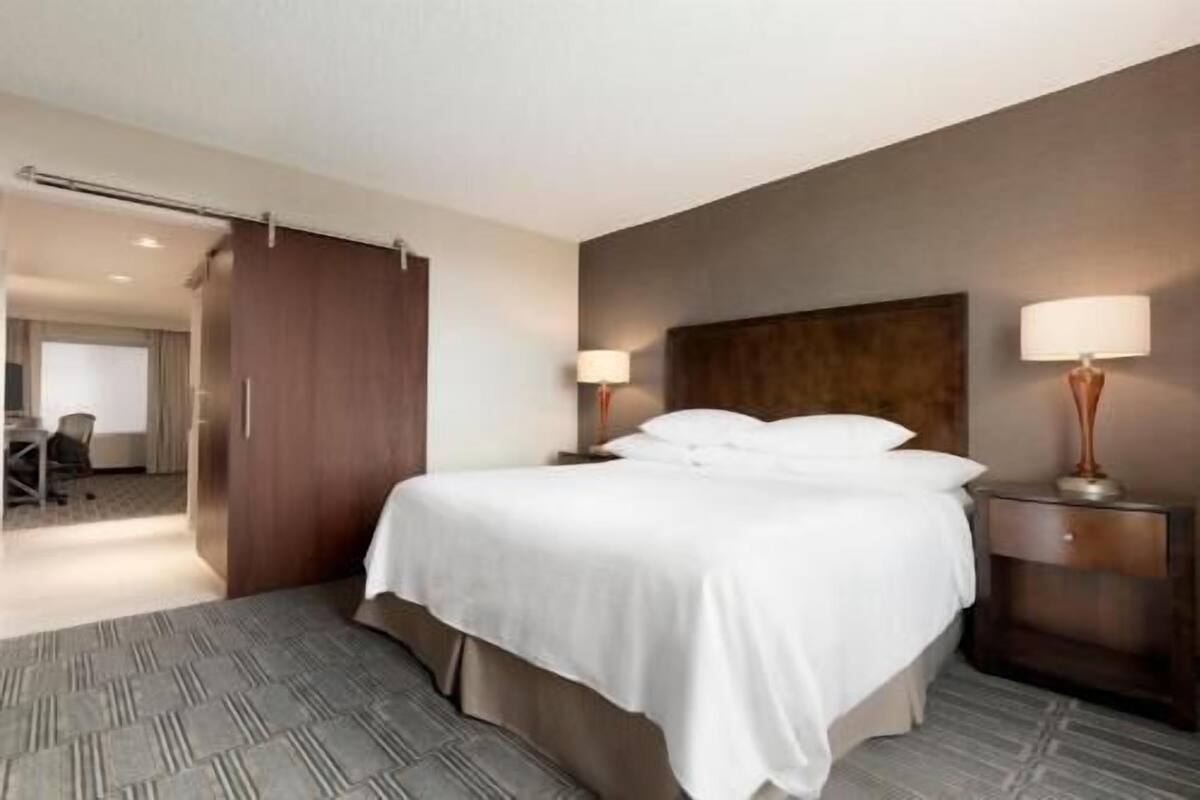 Une chambre d’hôtel avec un lit, deux lampes de chevet, une tête de lit en bois et un sol recouvert de moquette.
