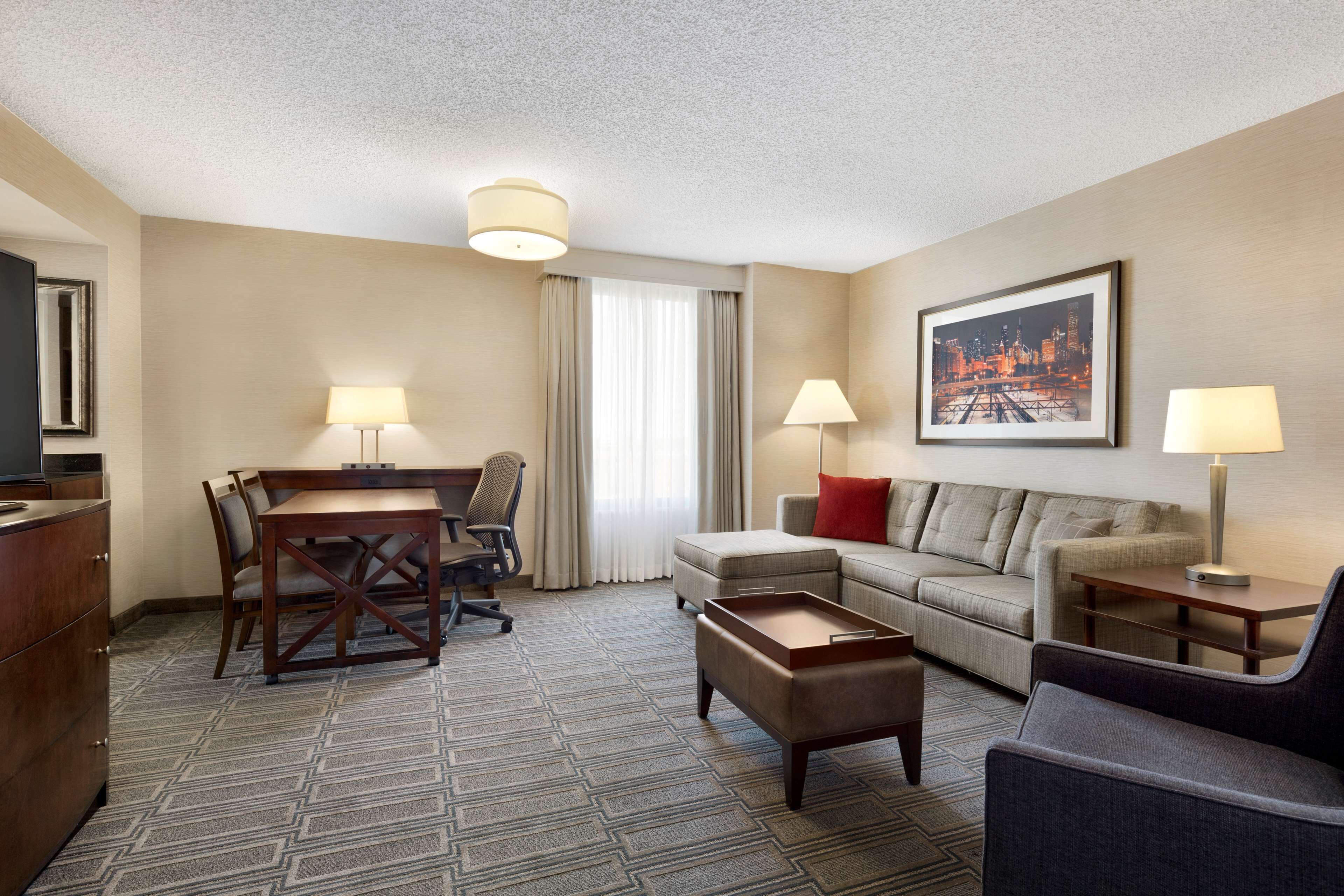 A hotel room with a dining table, two chairs, a sofa, a coffee table, and a TV.