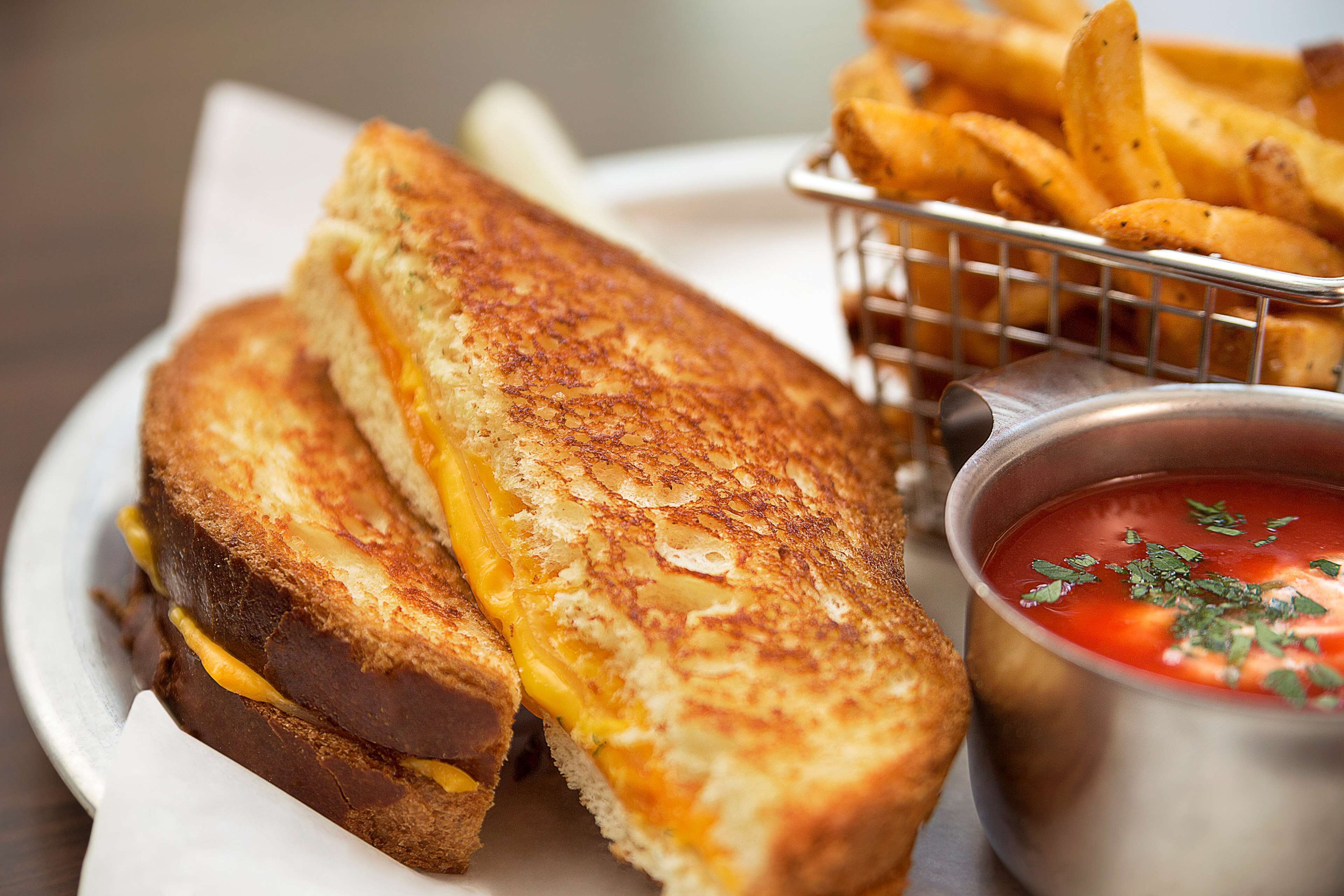 A grilled cheese sandwich, a basket of fries, and a bowl of tomato soup.