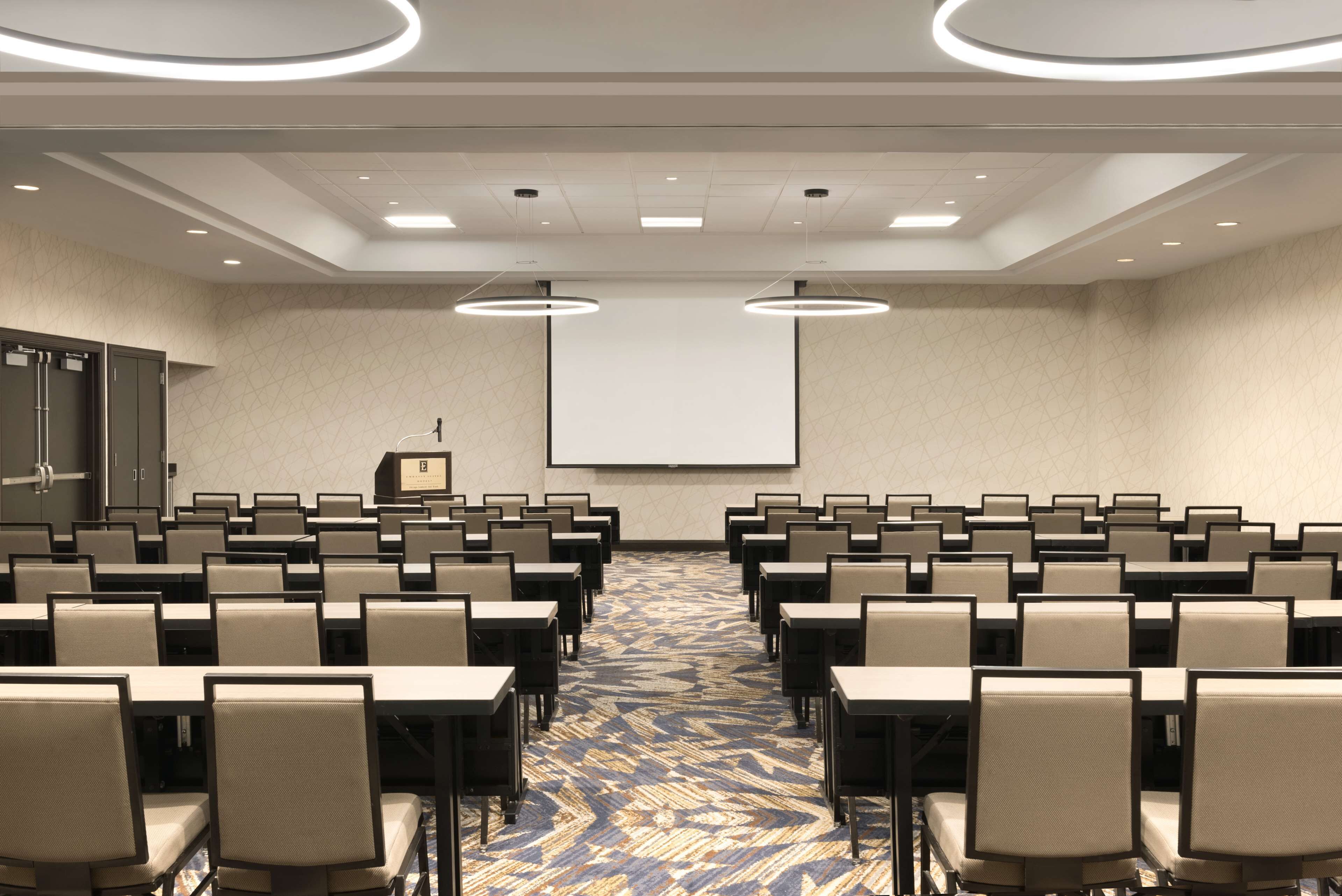 A conference room with rows of chairs, a projector screen, and a carpeted floor.