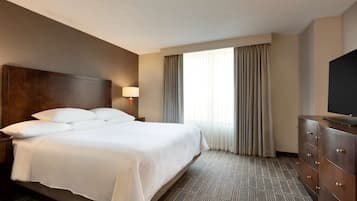 A hotel room with a large bed, a dresser, a television, and a window with curtains.