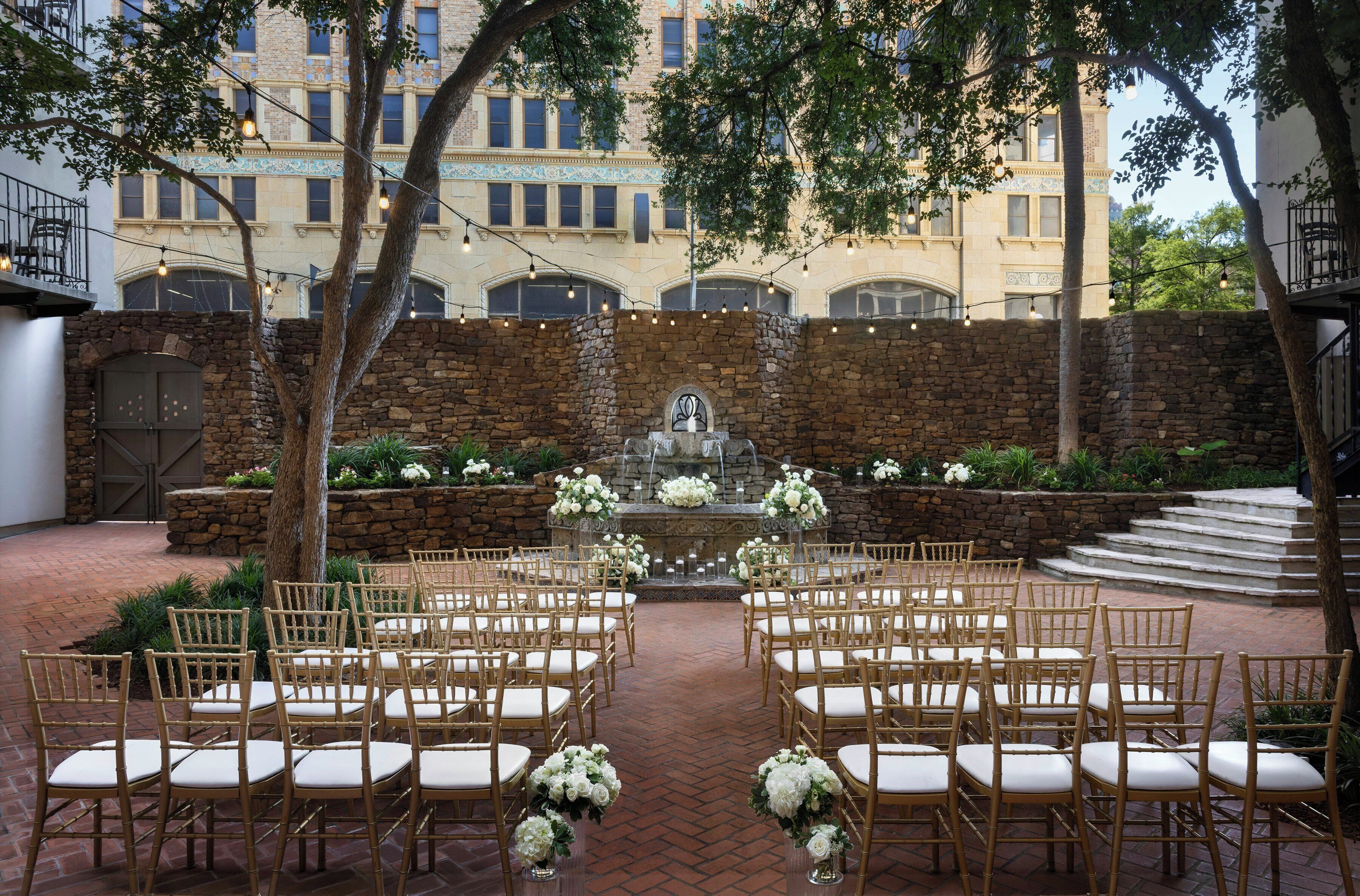 Un lieu de réception en plein air pour les mariages, avec des murs en pierre, une fontaine et des rangées de chaises en bois.