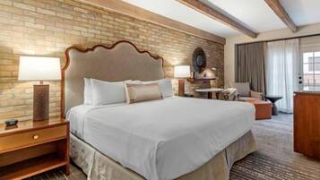 Habitación de hotel con una cama grande, cabecera de madera, pared de ladrillo y una mesita con lámpara.