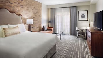 A hotel room with a large bed, a desk, a chair, a television, and a brick wall.