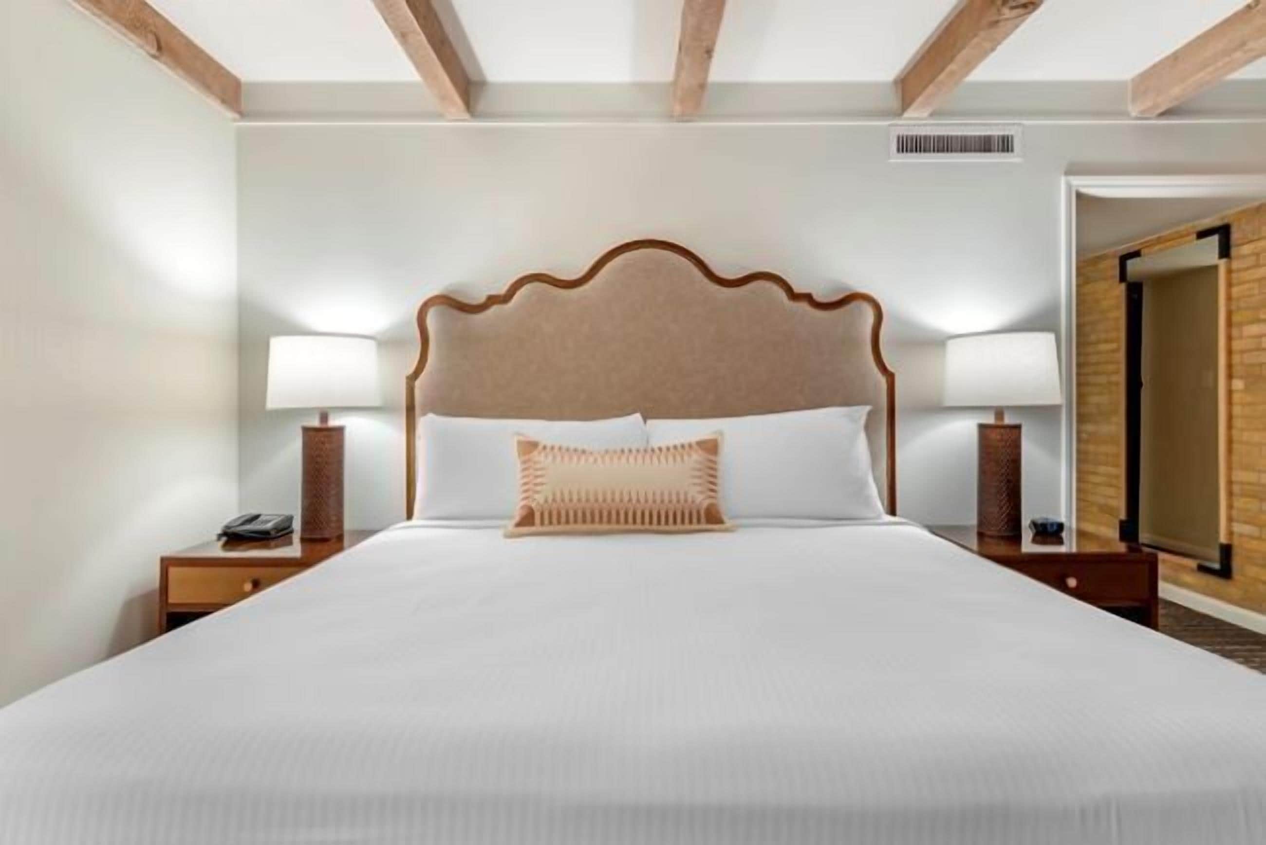 Una habitació d'hotel amb un llit gran, dues làmpades de nit, un panell de capçal de fusta i una petita taula de nit amb un telèfon.