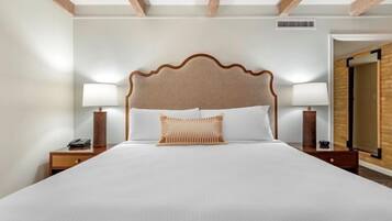 A hotel room with a large bed, two bedside lamps, a wooden headboard, and a small nightstand with a phone.