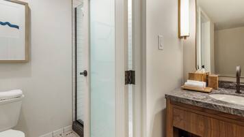 A modern bathroom with a toilet, a glass shower enclosure, a marble sink, and a wooden vanity.