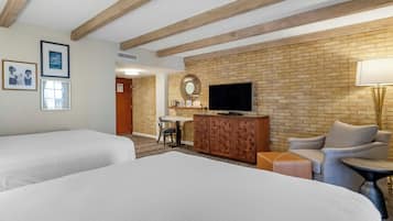 A hotel room with two beds, a TV, a brick wall, and a small table with a chair.