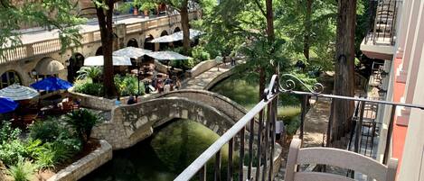 A balcony with a view of a canal, surrounded by greenery and a stone bridge.