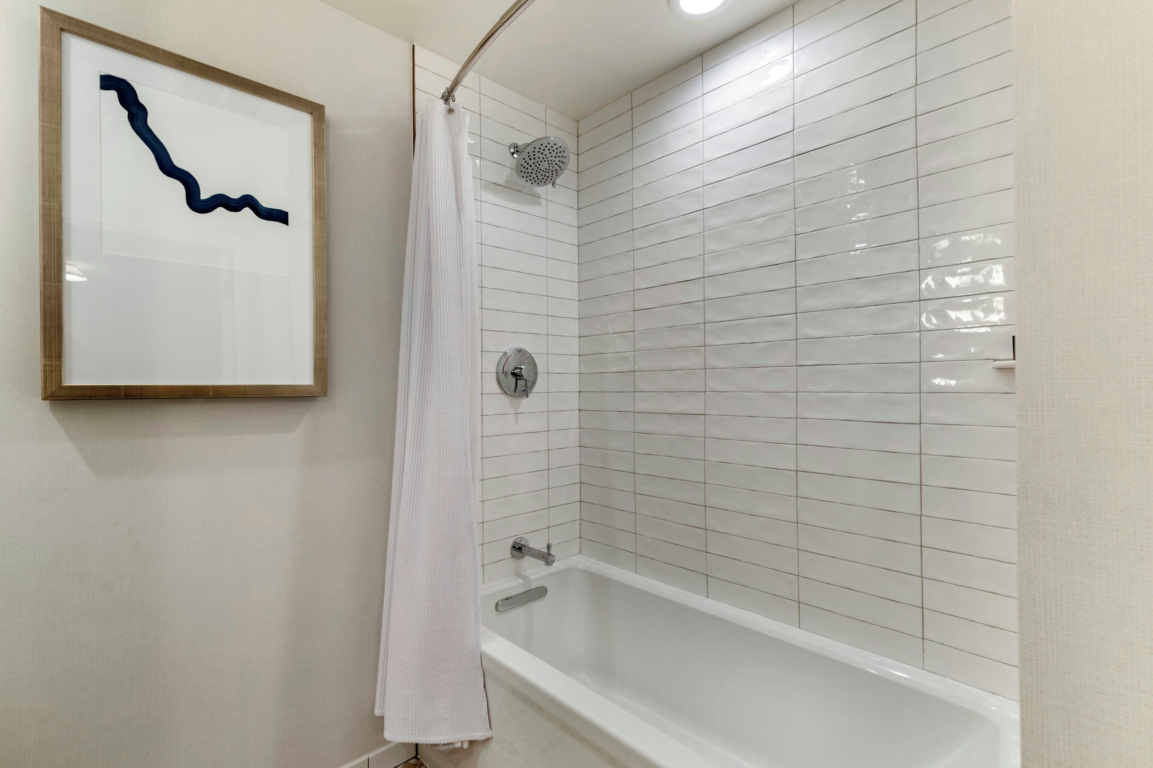 Un bagno con una vasca, un soffione doccia e un'opera d'arte incorniciata al muro.