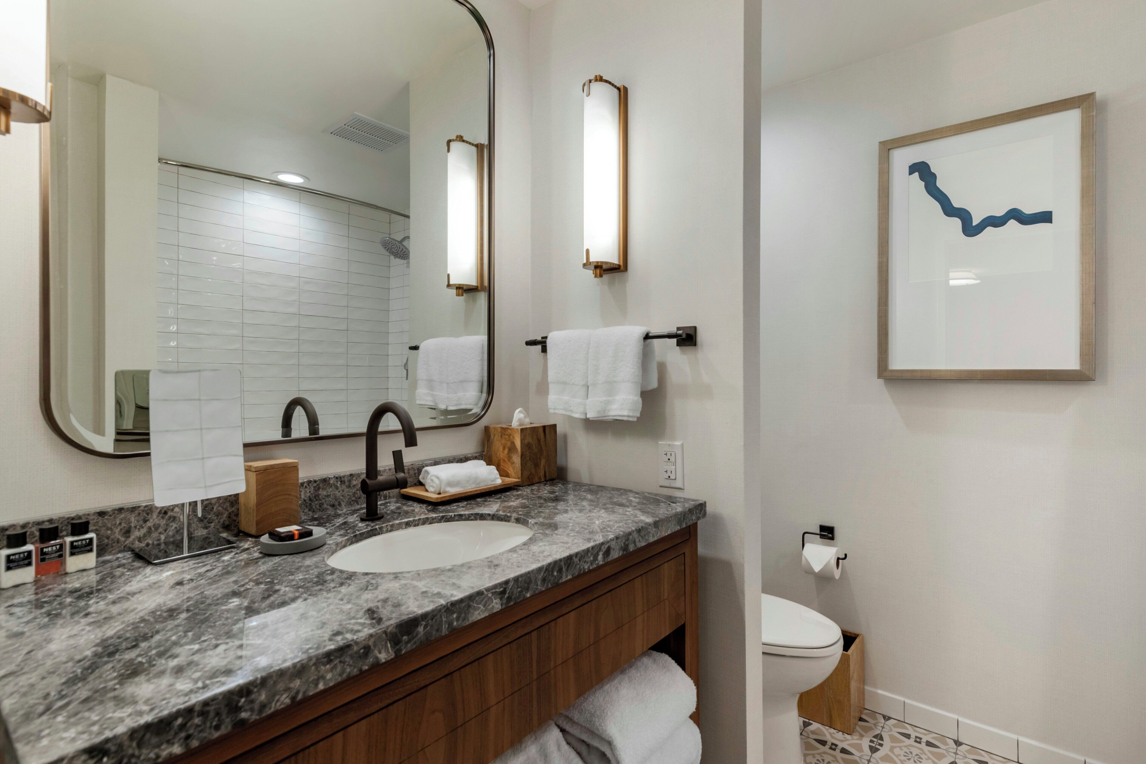 A bathroom with a marble sink, a mirror, a towel rack, a toilet, and a framed artwork on the wall.