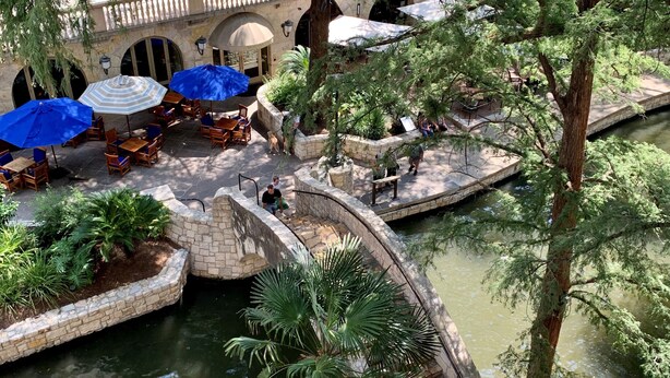 A courtyard with stone planters, a small water feature, and outdoor seating with umbrellas. - Omni La Mansion del Rio (San Antonio)