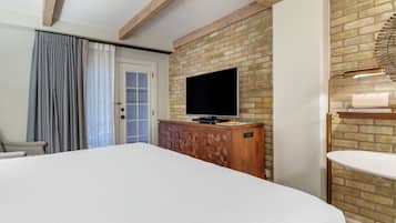 Habitación de hotel con una cama grande, un televisor montado en una pared de ladrillo, un armario de madera y una mesita de noche con una lámpara.