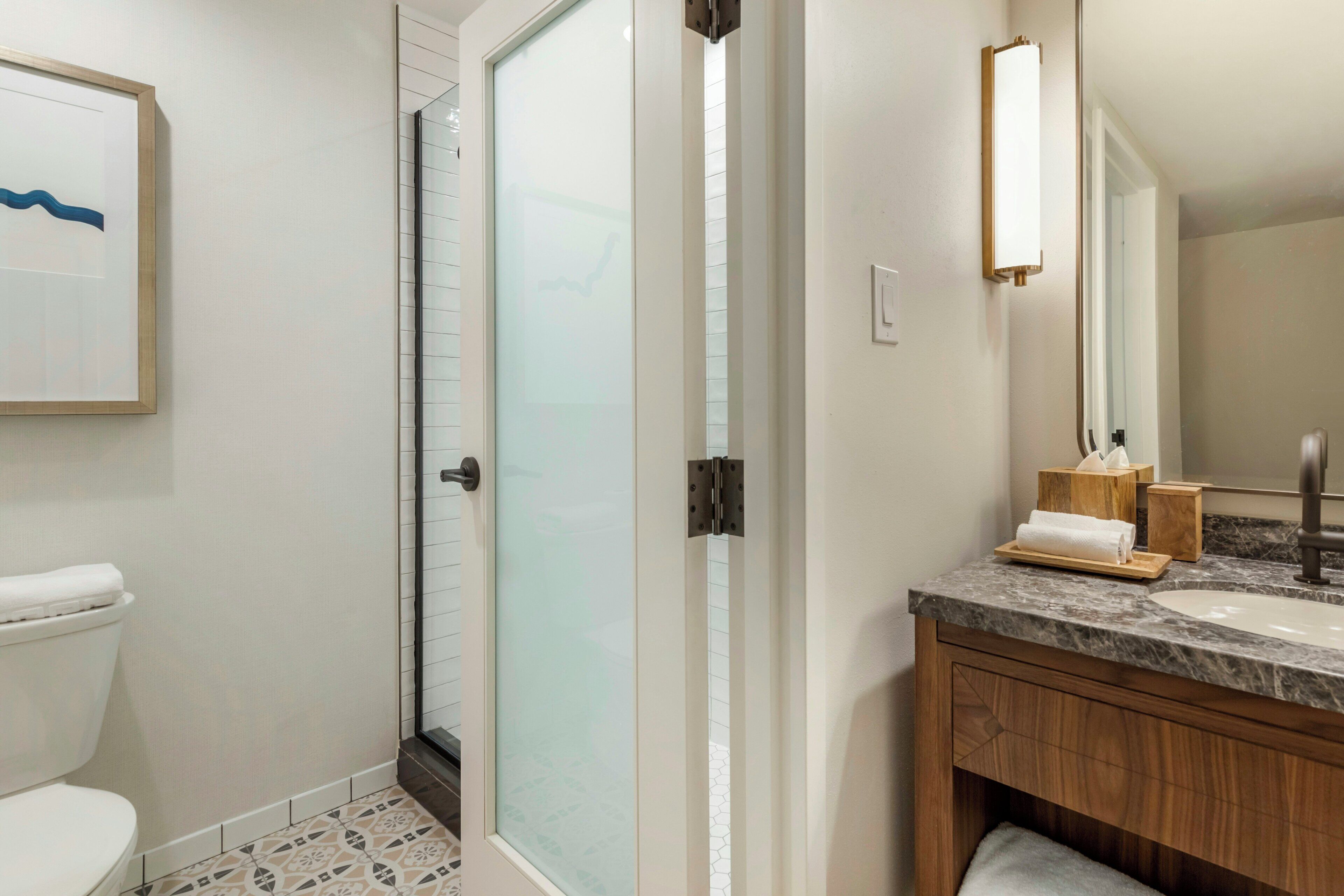 A bathroom with a toilet, a shower with frosted glass doors, a sink with a marble countertop, and a wooden vanity.