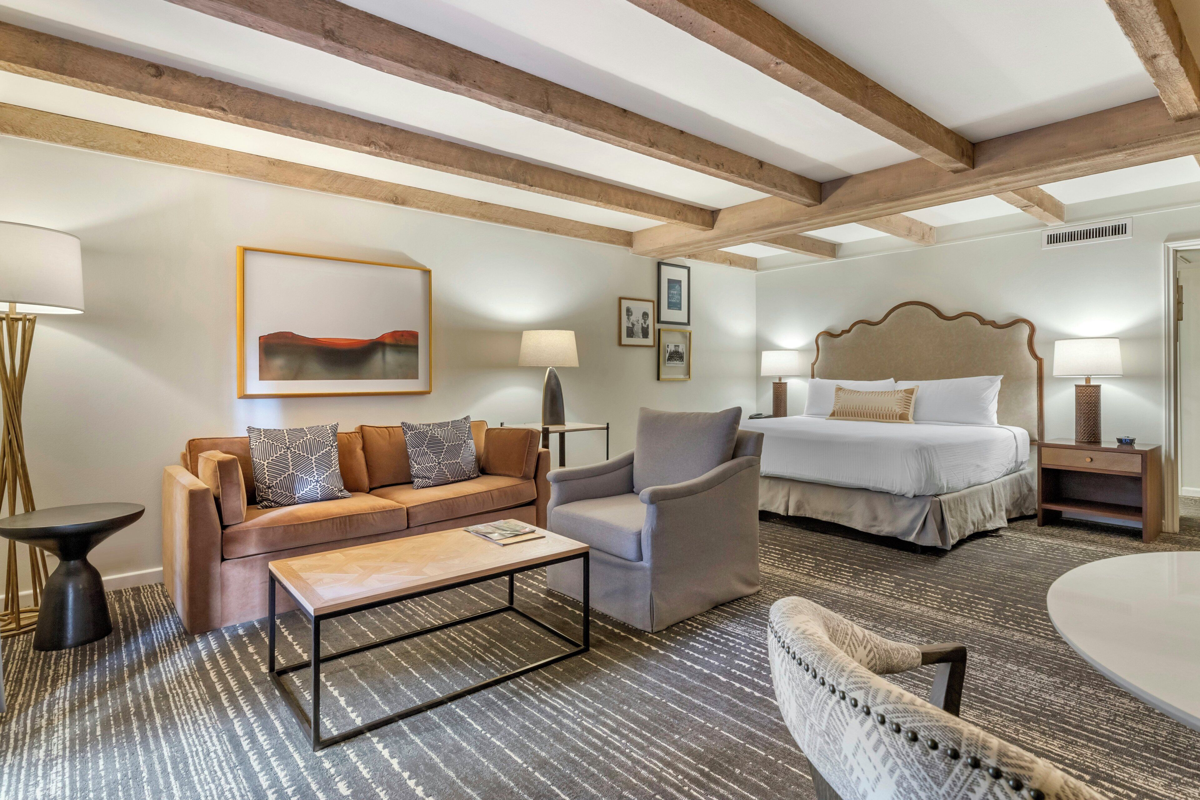Una habitación de hotel con una cama, un sofá, un sillón, una mesa de centro y una lámpara.