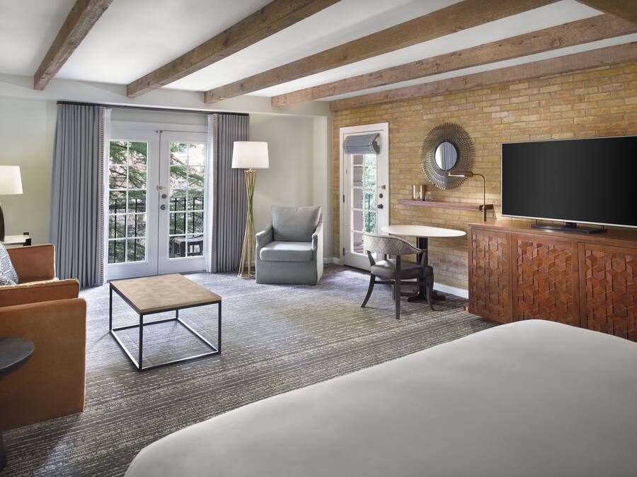 Ein Hotelzimmer mit einem großen Bett, einer Sitzecke inklusive Sofa und Sesselsowie einem kleinen Tisch, einem Fernseher und einer Ziegelwand.