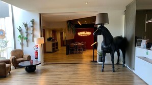 Un vestíbulo de hotel con piso de madera, una estatua de un caballo negro, un letrero de neón y un mostrador de recepción.
