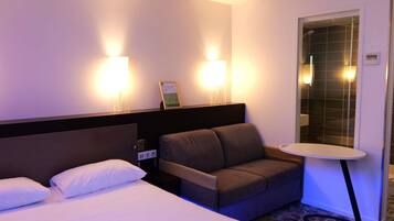 A hotel room with a bed, a sofa, a small table, and two wall-mounted lights.