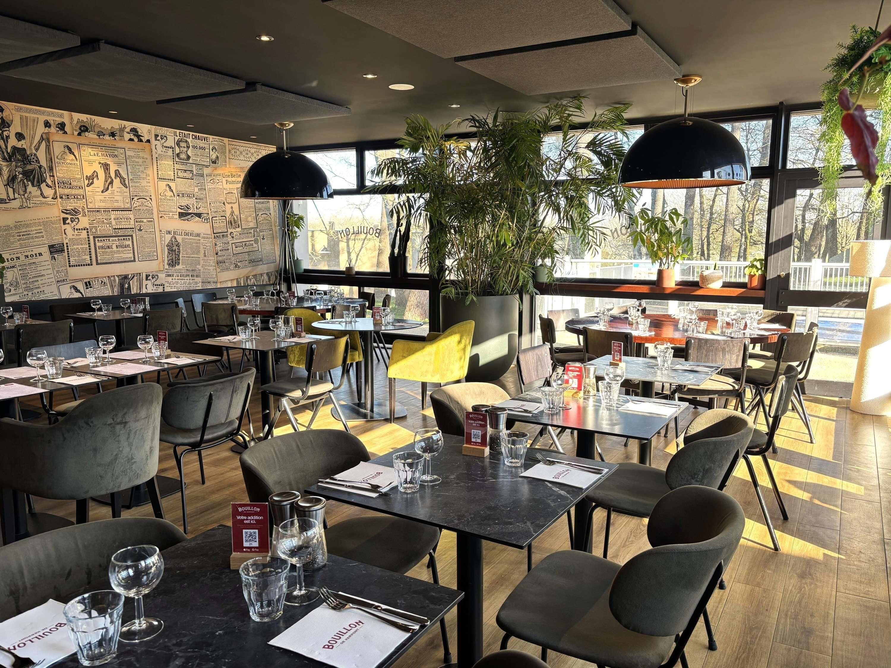 A restaurant with tables set for dining, a menu stand, and a wall with vintage posters.