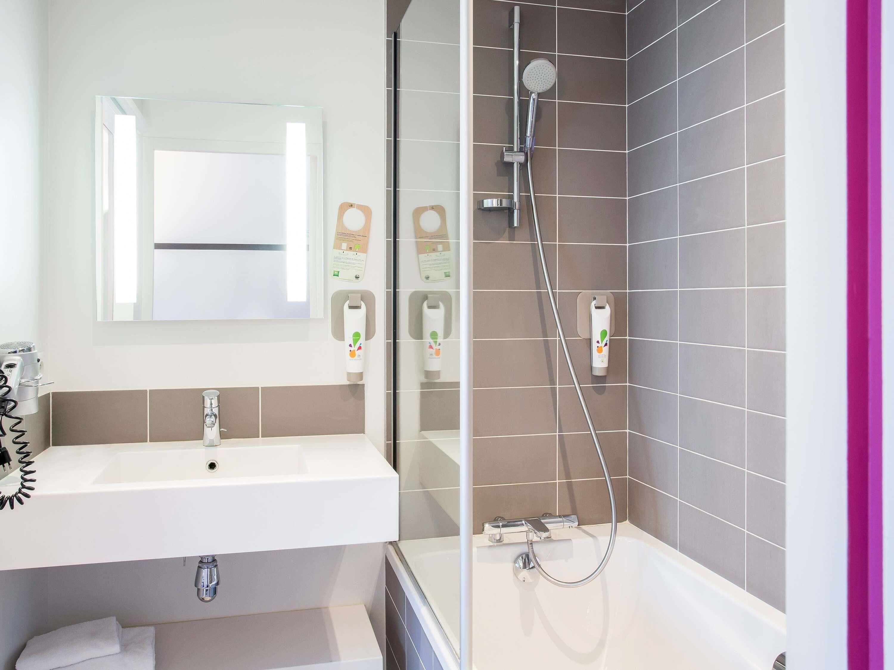 A modern bathroom with a sink, mirror, shower, and hand dryer.