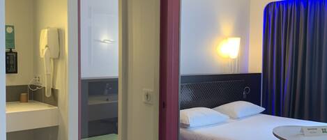 A hotel room with a bed, bedside table, lamp, and a bathroom with a toilet and sink.