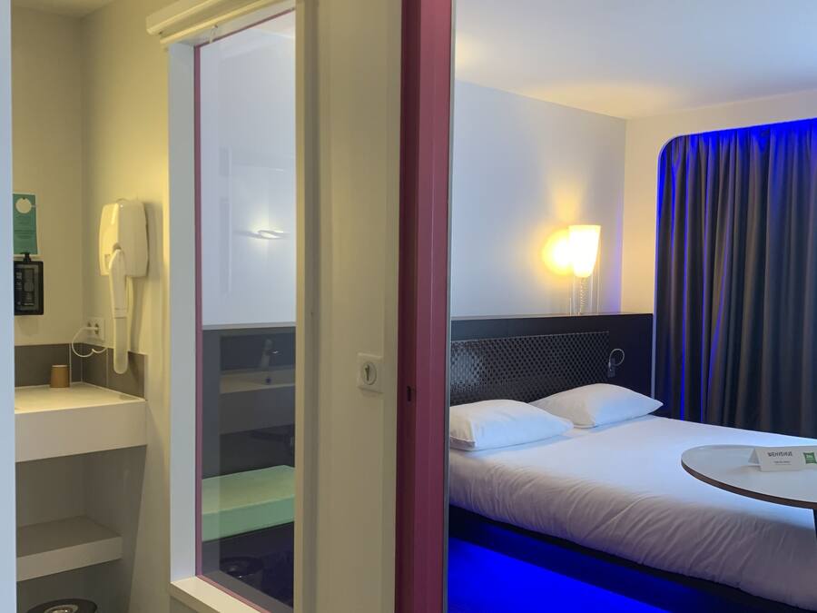 Een hotelkamer met een bed, nachtkastje, lamp en een badkamer met toilet en wastafel.