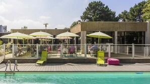 Un área junto a la piscina con sillones de descanso, sombrillas y una piscina.