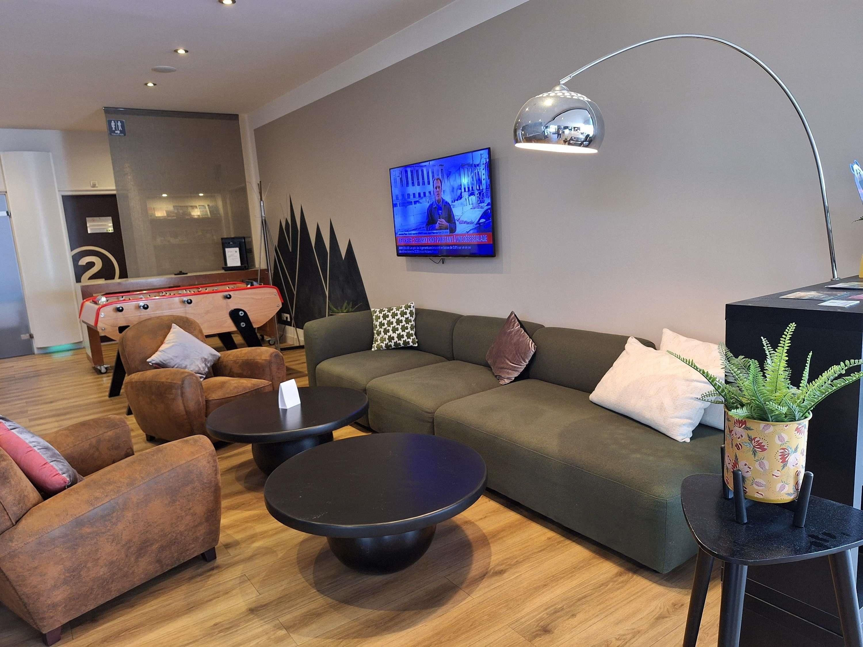 Een moderne woonkamer met een bank, fauteuils, een salontafel, een televisie en een tafelvoetbaltafel.