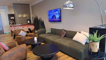 Een moderne woonkamer met een bank, fauteuils, een salontafel, een televisie en een tafelvoetbaltafel.