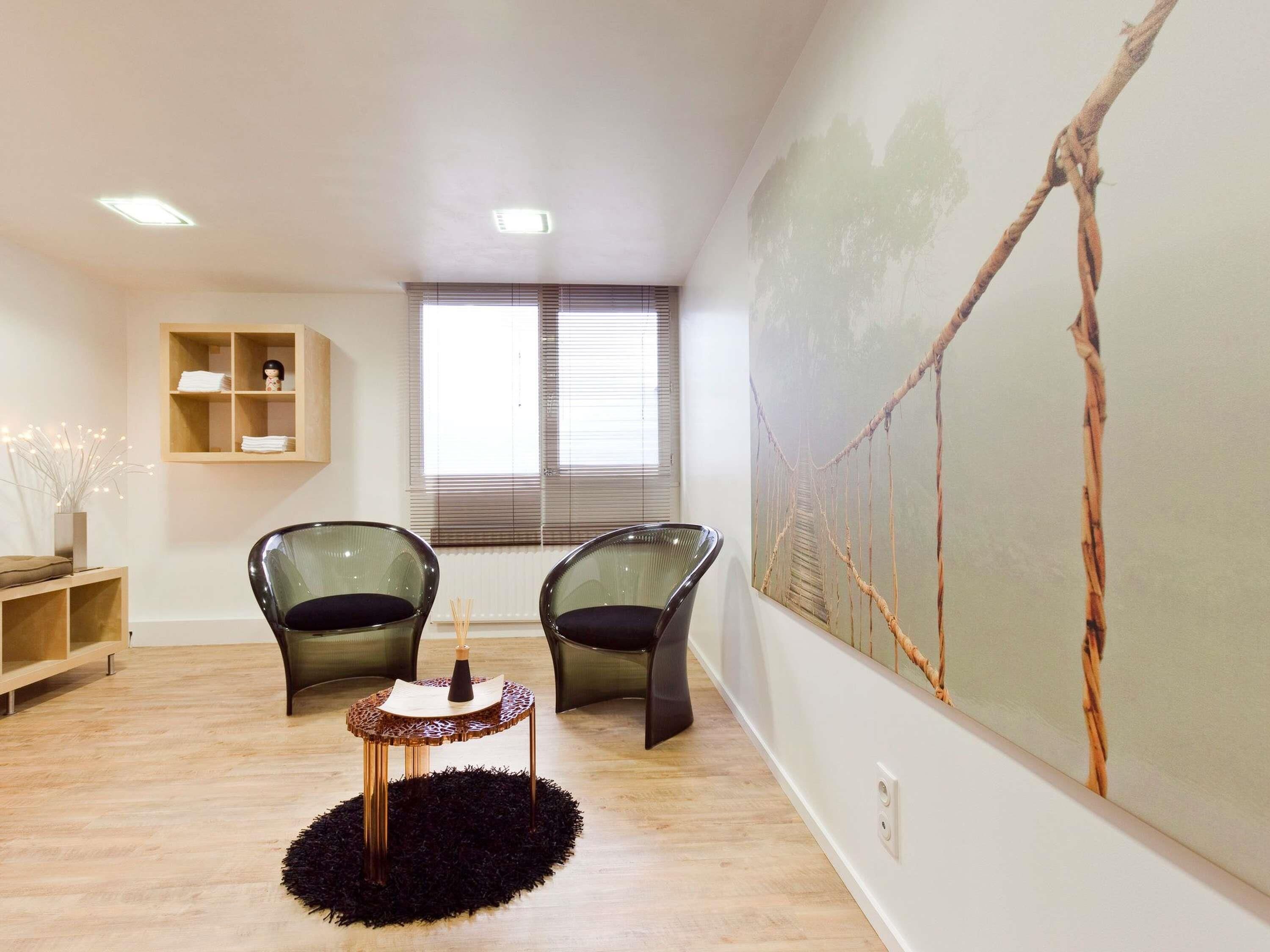 A room with two chairs, a small table, a shelf, and a large painting on the wall.