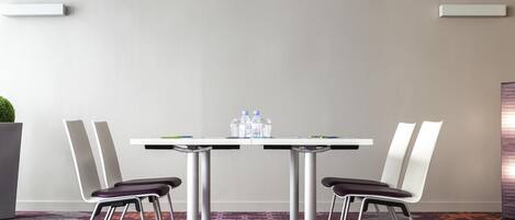 A conference room with a white table, two chairs, a water dispenser, and a patterned carpet.