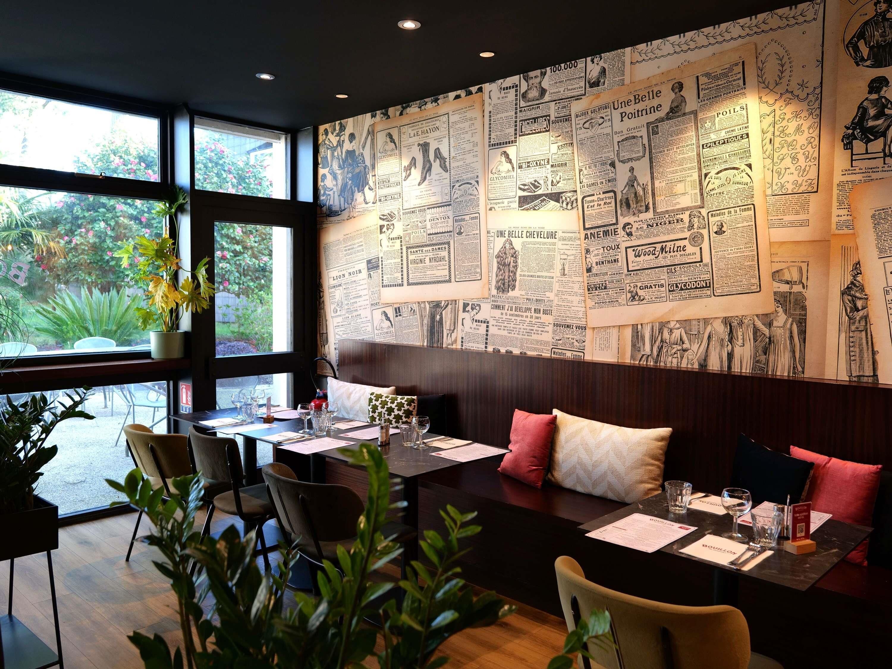 A restaurant with a wall of vintage newspaper clippings, large windows, and indoor plants.