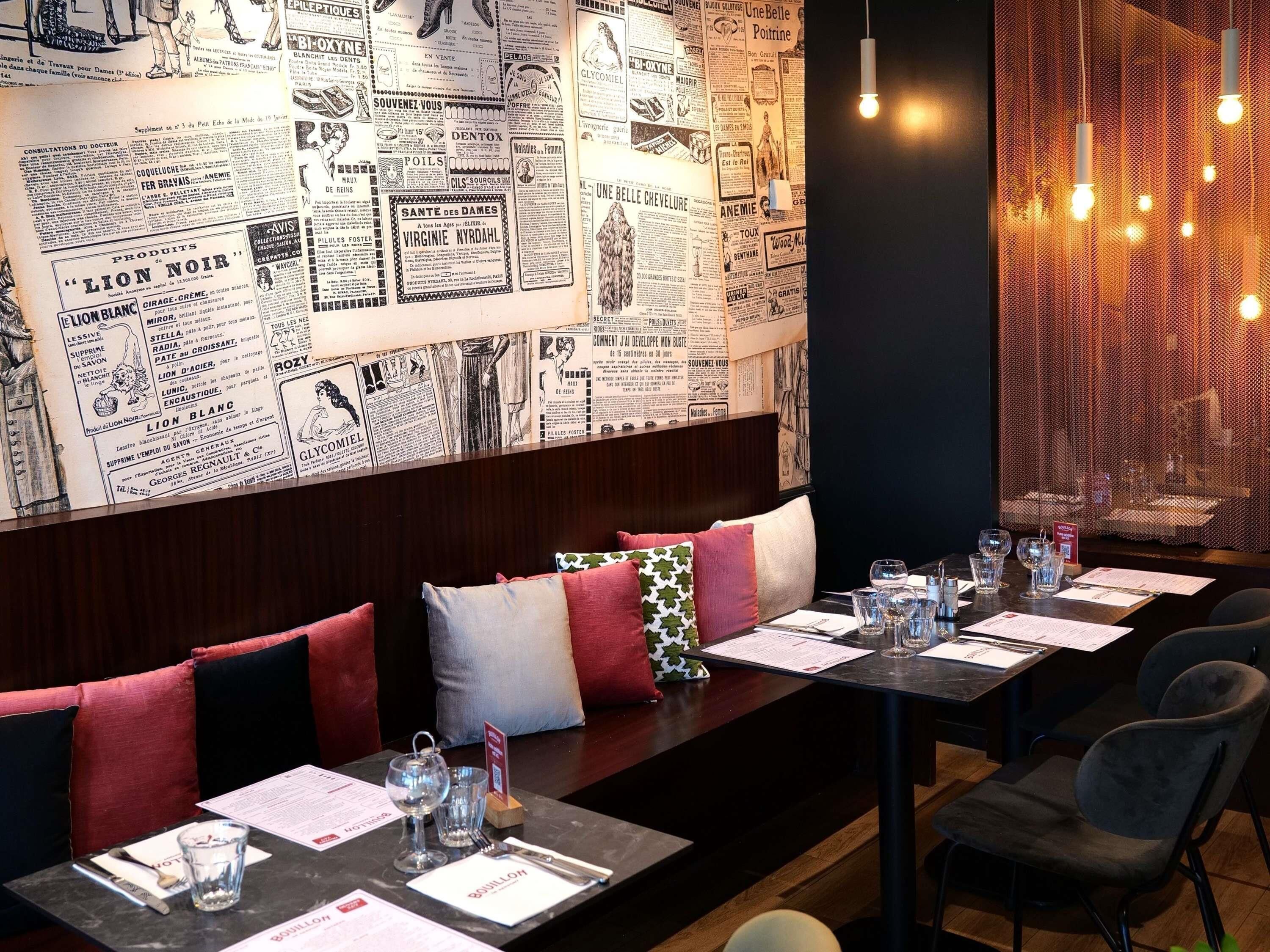 Un restaurante con una pared de periódicos antiguos, una larga mesa de comedor con sillas y una luminaria cálida.